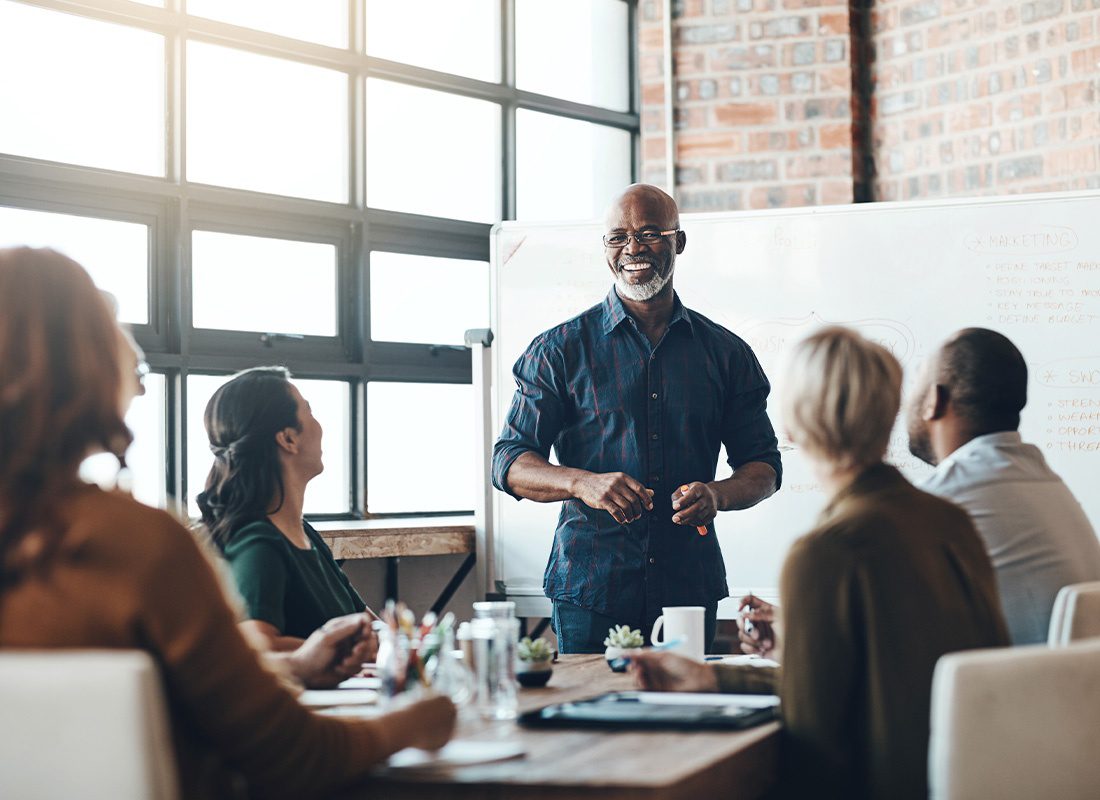 Insurance Solutions - Smiling Businessman Giving a Presentation to His Colleagues in a Boardroom Meeting