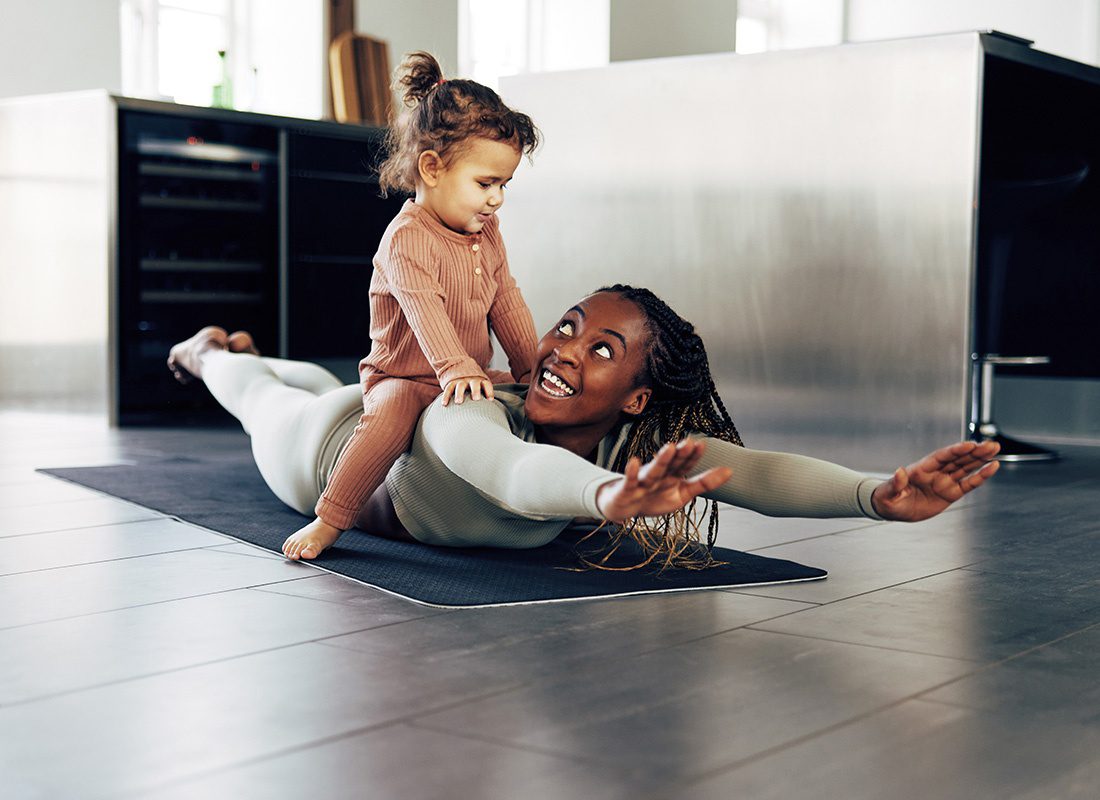 Health Insurance - Smiling Mother and Daughter Playing Together at Home While Exercising on the Floor